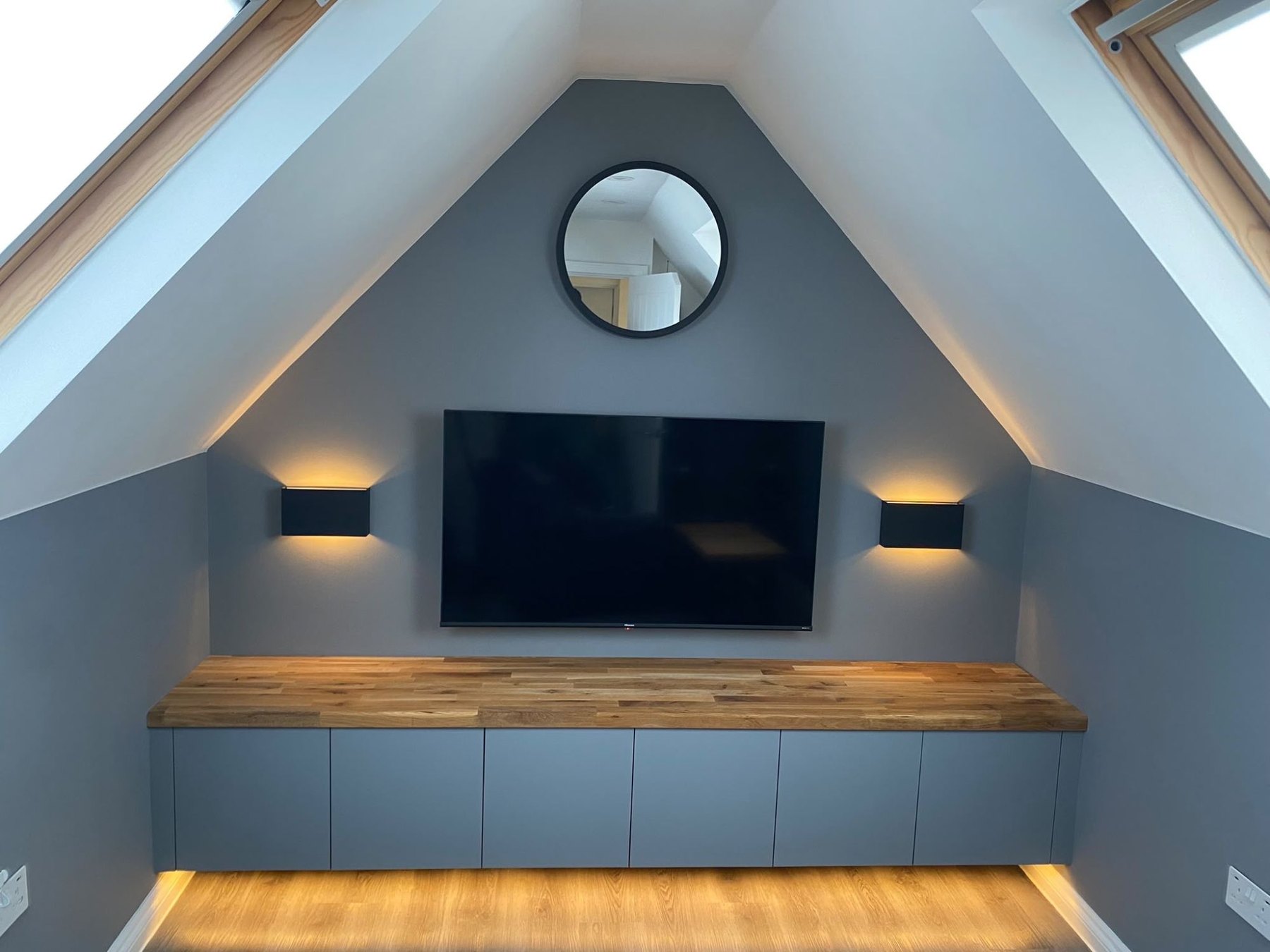 Fitted loft unit with lighting under the cupboards and wall lights either side of the television, built into the eaves