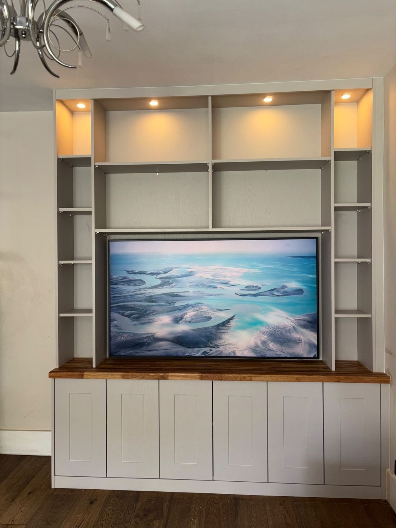 Painted media wall with a recessed television, open shelving lit from above, a solid oak worktop and shaker cupboards below