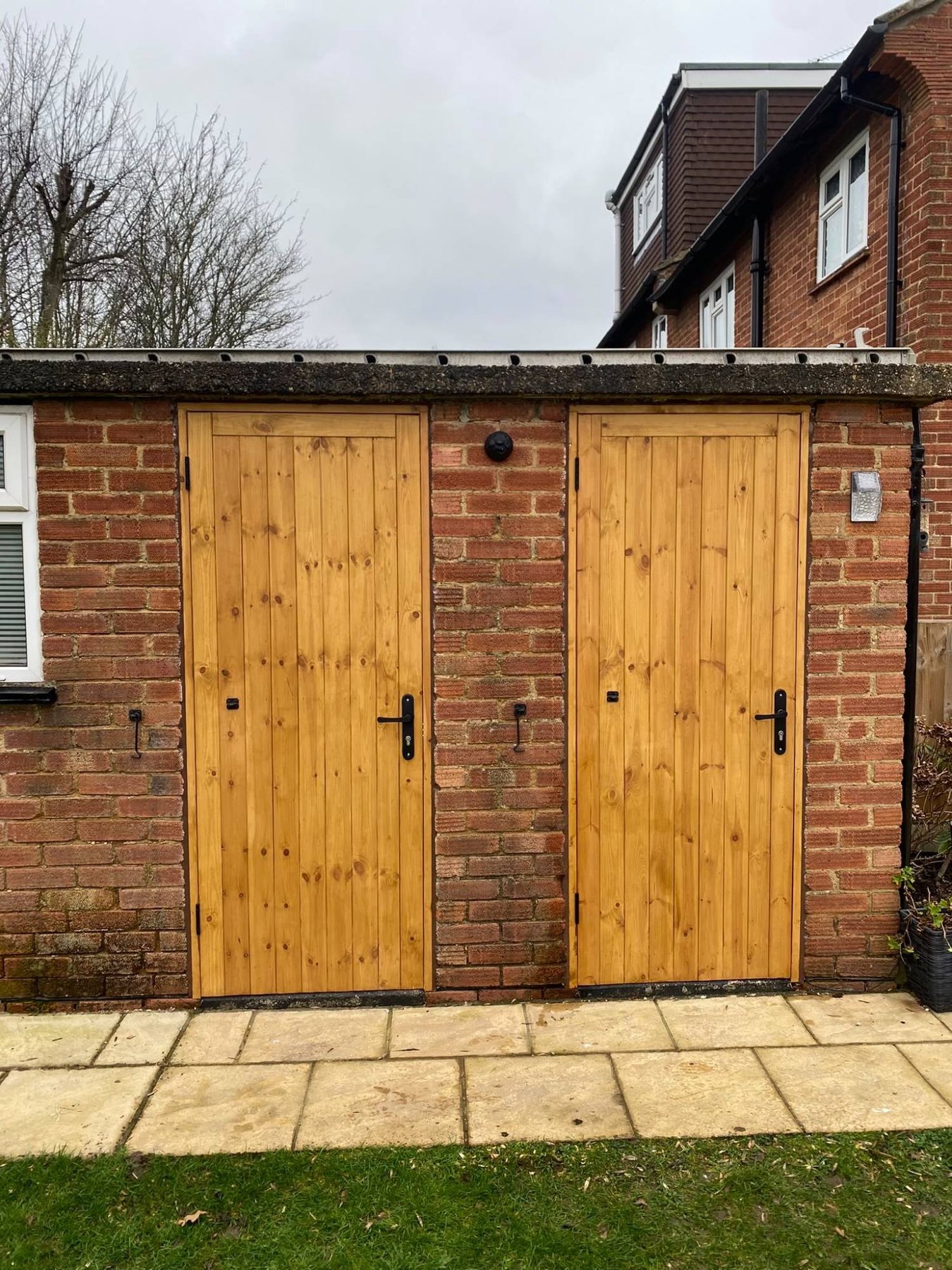A pair of solid timber ledged doors hung in a brick outbuilding, with black ironmongery and a treated finish