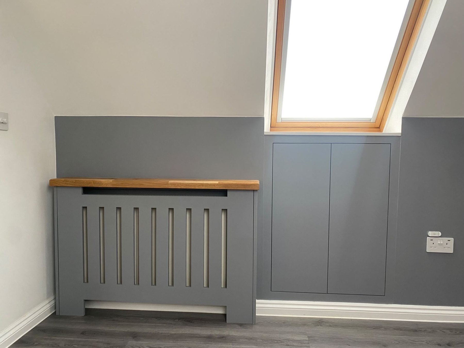 Slatted radiator cover with a solid oak top, alongside fitted cupboards built into the slope of a loft room
